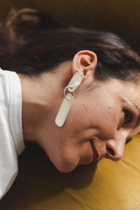 Mujer usando aretes largos de plata sobre fondo amarillo